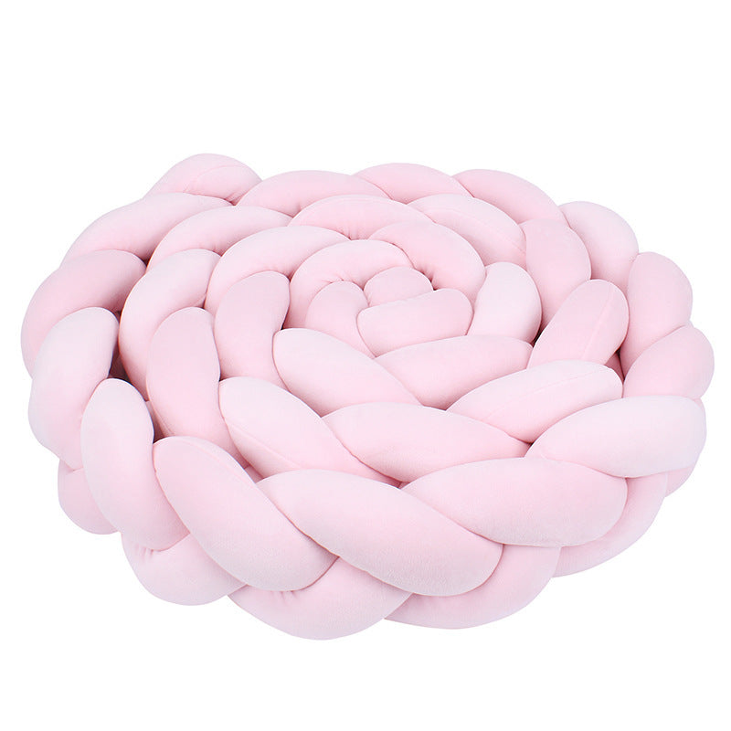 Rožinė, minkšta, pintinė pagalvė, suformuota spiralės pavidalu.