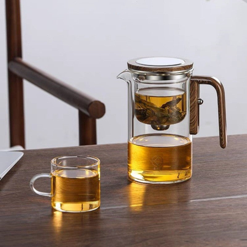 Stiklinis arbatinukas su mediniu rankenėle, šviesiai geltonos arbatos puodelis.