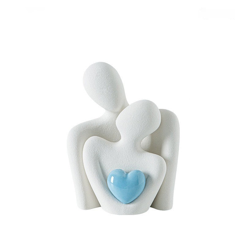 Balta keraminė skulptūra, vaizduojanti porą su mėlynu širdies akcentu.